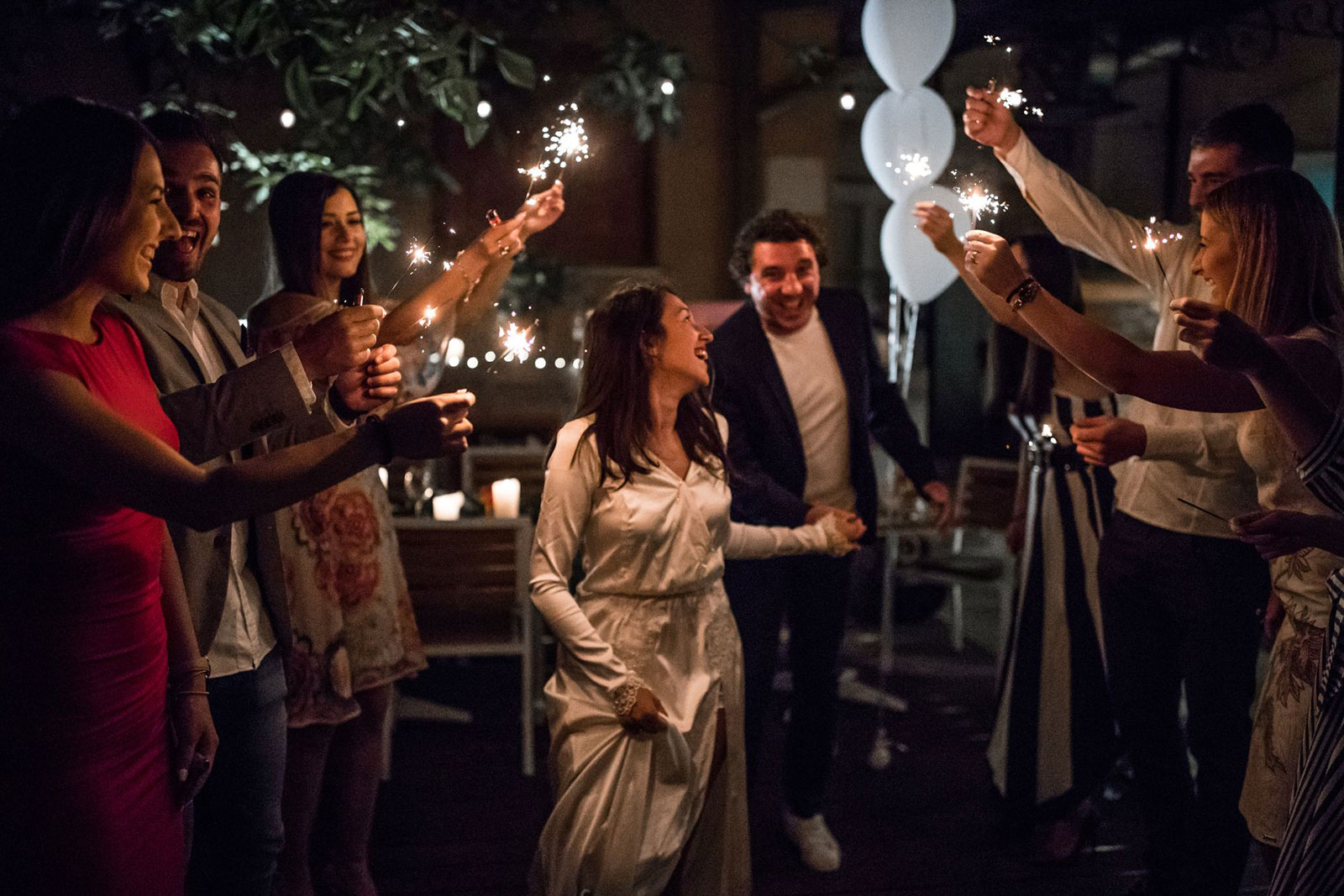 Bride and groom being serenaded by adult guests with sparklers
