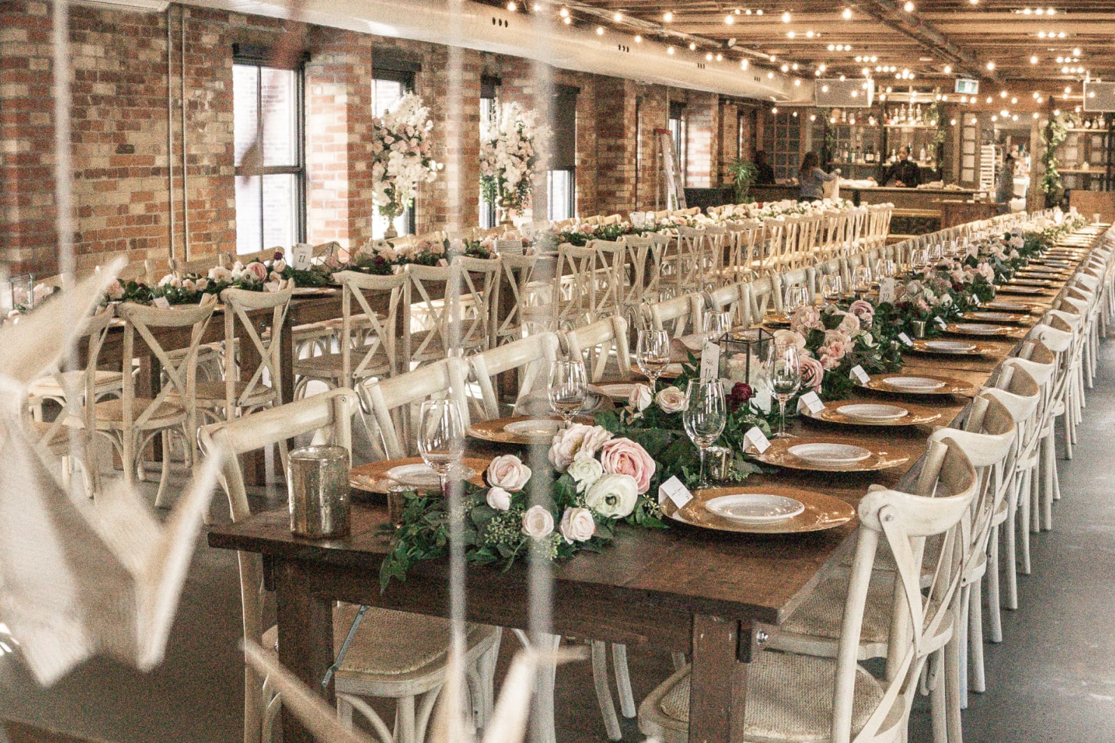 An indoor wedding reception hall with two long tables decorated with fairy lights and flowers