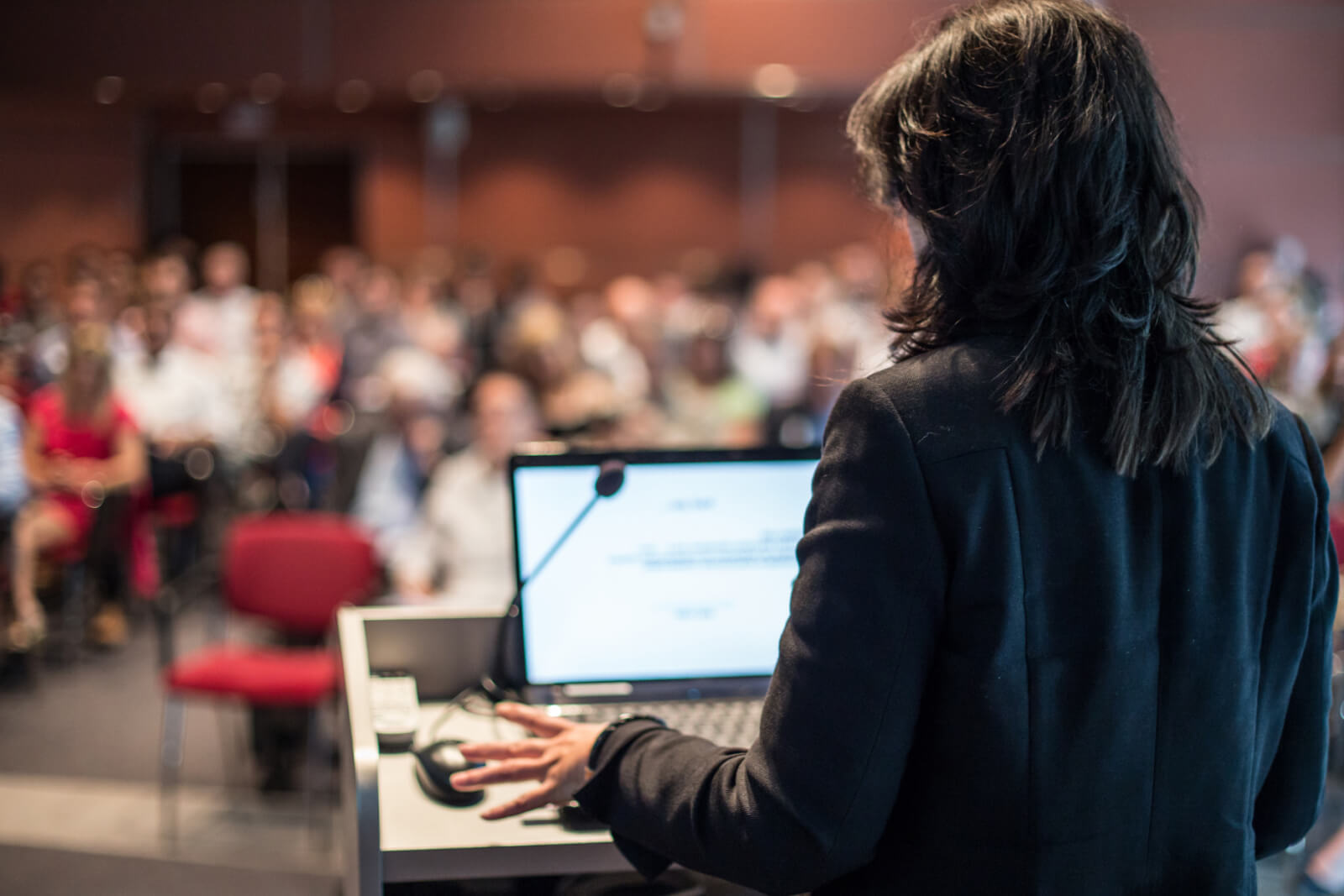 A guest speaker addresses a large room full of people at a company event