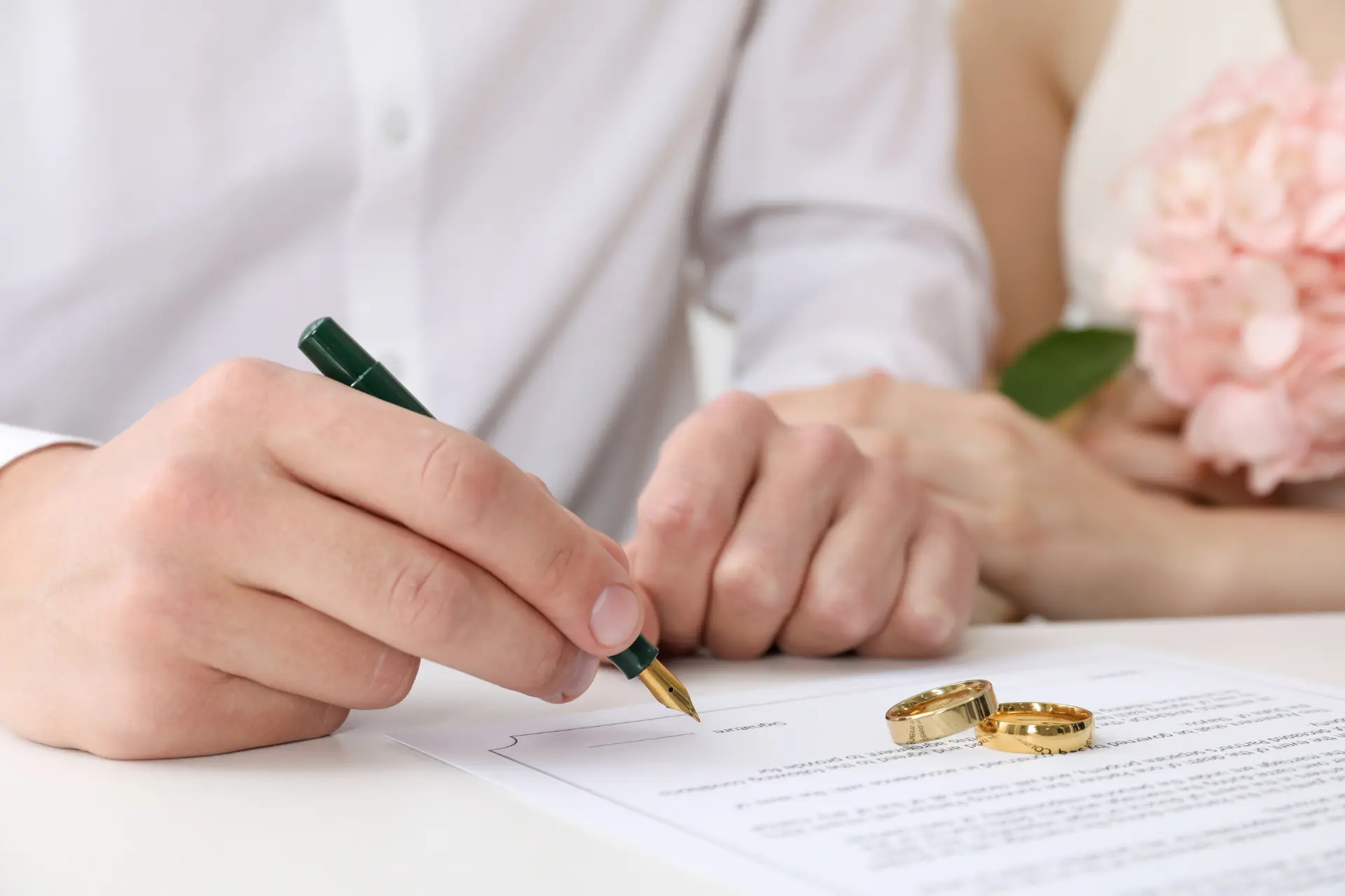 Close-up of a couple signing a marriage licence with a pair of rings on top of it 