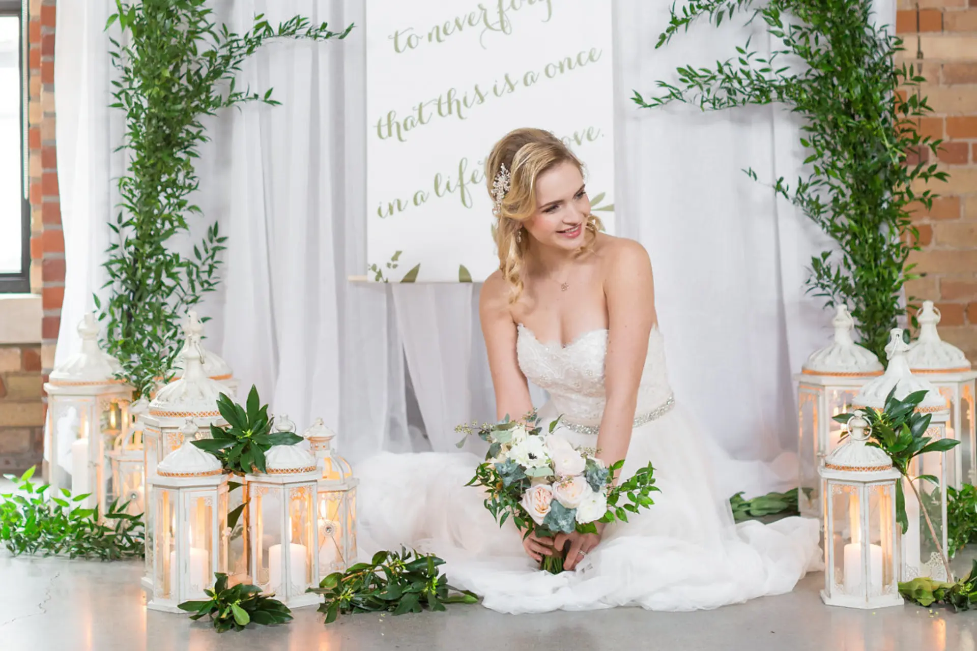 A beautiful bride sitting on the floor of The Loft on King, surrounded by greenery and candles